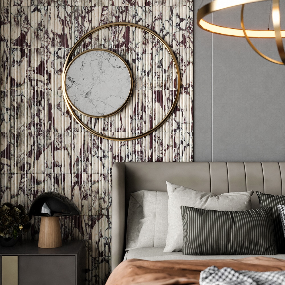 Calacatta viola fluted marble tile used as full bedroom accent wall with dramatic burgundy and violet veining on vertical ridged surface, gold circular mirror with white marble inset, upholstered bed headboard and gold ring pendant light