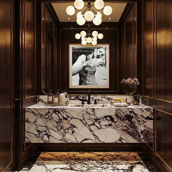 Calacatta viola marble vanity top and backsplash in commercial powder room with bold burgundy and violet veining, dark walnut paneling with gold trim detail, globe chandelier with brass arms, black matte faucet and luxury editorial photograph above vanity